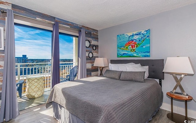 bedroom with a textured ceiling, access to exterior, a water view, and hardwood / wood-style floors