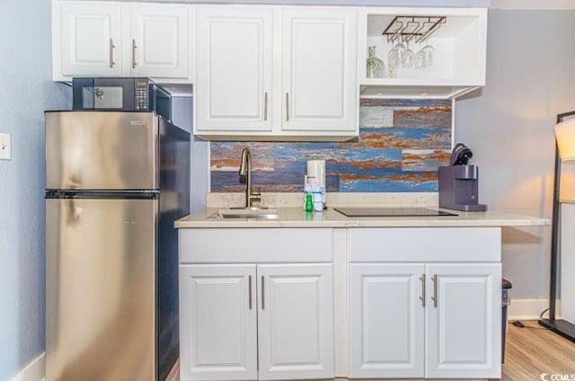 kitchen featuring backsplash, black electric stovetop, sink, stainless steel refrigerator, and white cabinetry