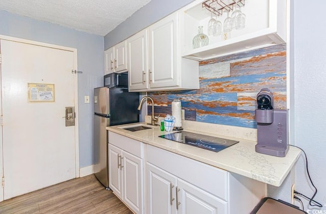 kitchen with black electric stovetop, decorative backsplash, a textured ceiling, white cabinets, and sink