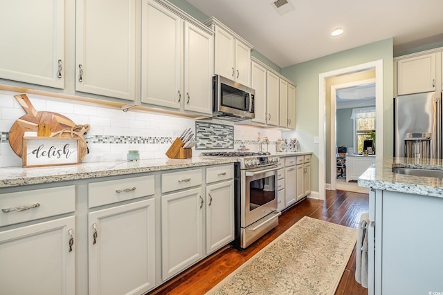 kitchen featuring backsplash, dark hardwood / wood-style floors, white cabinetry, light stone countertops, and appliances with stainless steel finishes