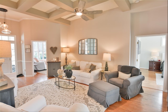 living room with coffered ceiling, light wood-type flooring, beamed ceiling, ceiling fan, and a high ceiling