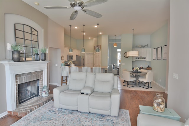 living room featuring ceiling fan, a fireplace, and light wood-type flooring