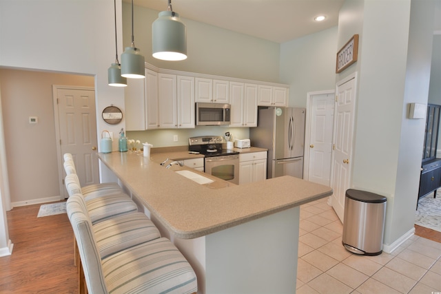 kitchen with appliances with stainless steel finishes, hanging light fixtures, a towering ceiling, a kitchen bar, and kitchen peninsula