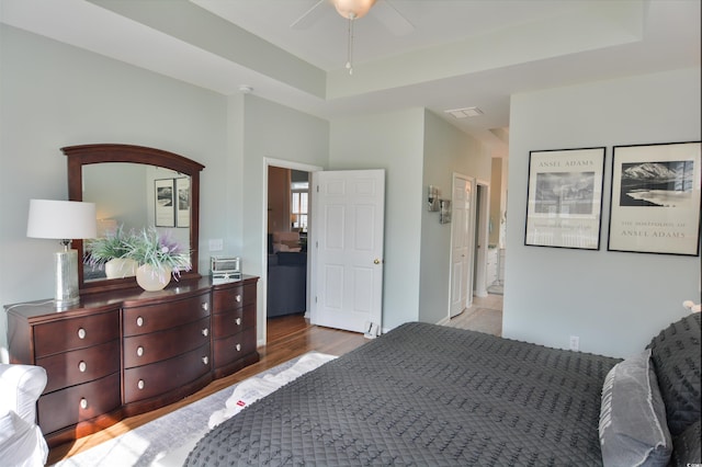 bedroom with ensuite bathroom, light hardwood / wood-style flooring, and a tray ceiling