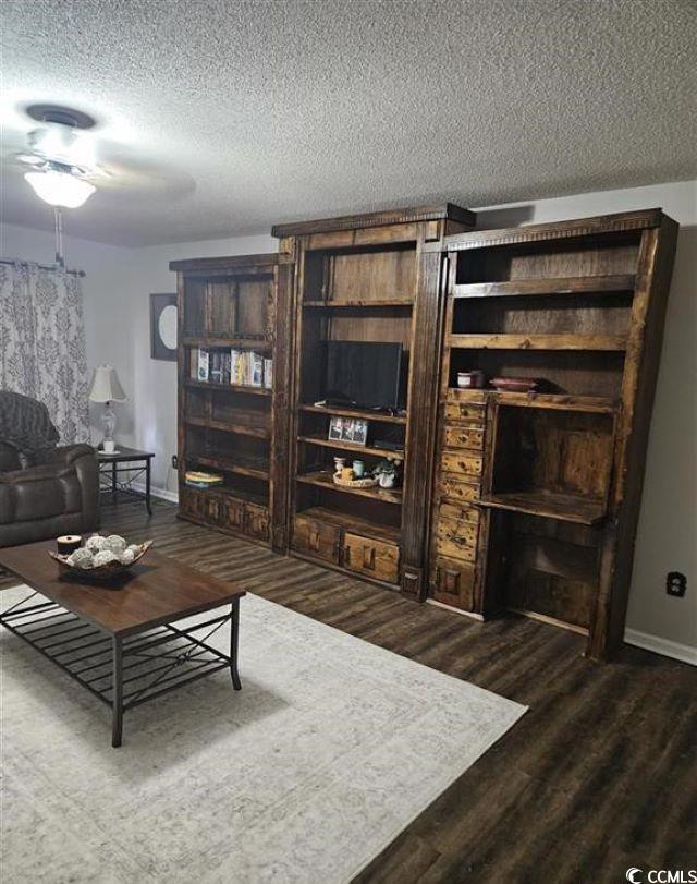 living area featuring a textured ceiling, baseboards, and wood finished floors