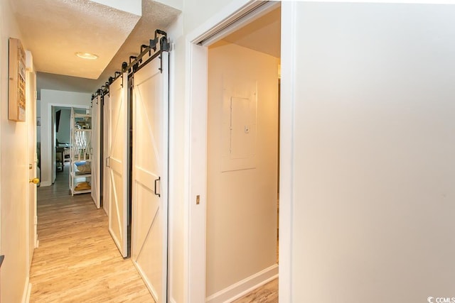 corridor featuring a barn door, a textured ceiling, and light wood-type flooring