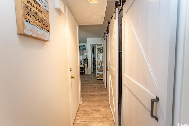 corridor with a barn door, a textured ceiling, and light wood-type flooring