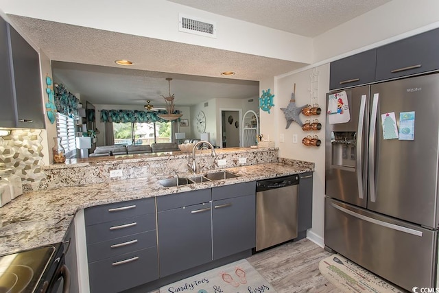 kitchen with light stone counters, stainless steel appliances, sink, and a textured ceiling