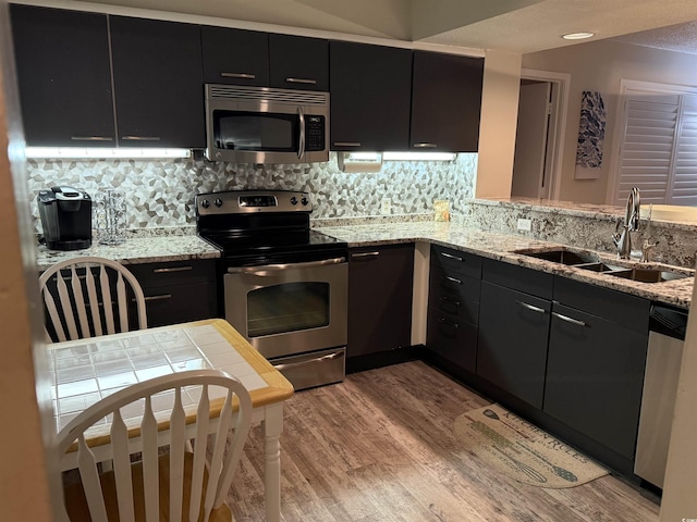 kitchen with sink, light hardwood / wood-style flooring, appliances with stainless steel finishes, light stone countertops, and backsplash