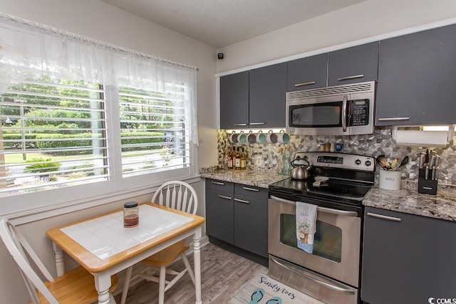 kitchen featuring light stone counters, a textured ceiling, appliances with stainless steel finishes, light hardwood / wood-style floors, and decorative backsplash