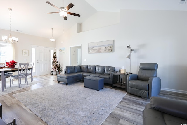 living room with light wood-type flooring, ceiling fan with notable chandelier, and high vaulted ceiling