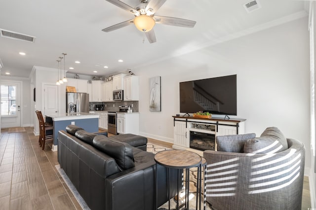 living room with ornamental molding, ceiling fan, and light hardwood / wood-style floors