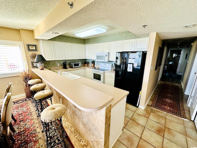 kitchen with kitchen peninsula, a breakfast bar area, white appliances, white cabinets, and sink