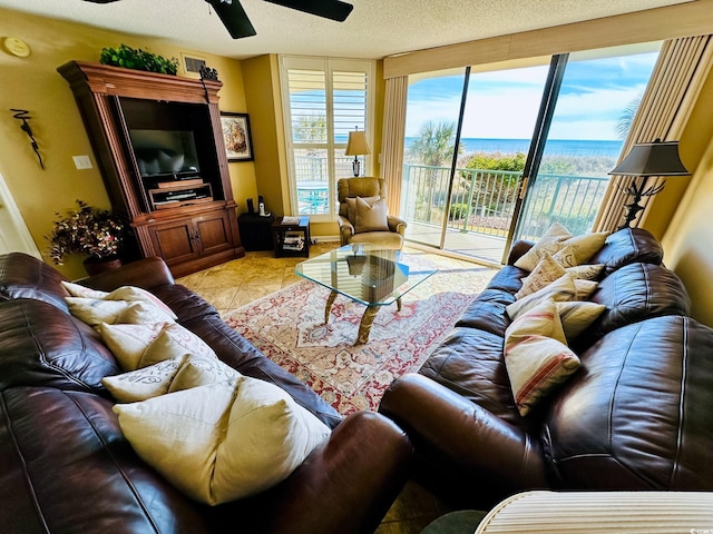 tiled living room featuring a textured ceiling, ceiling fan, and a water view