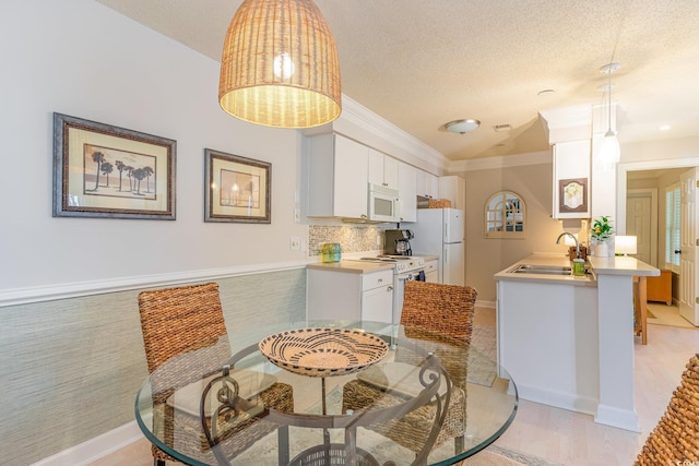 dining area featuring sink, light wood-type flooring, ornamental molding, and a textured ceiling