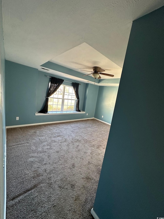 empty room with carpet, a textured ceiling, ceiling fan, and a tray ceiling