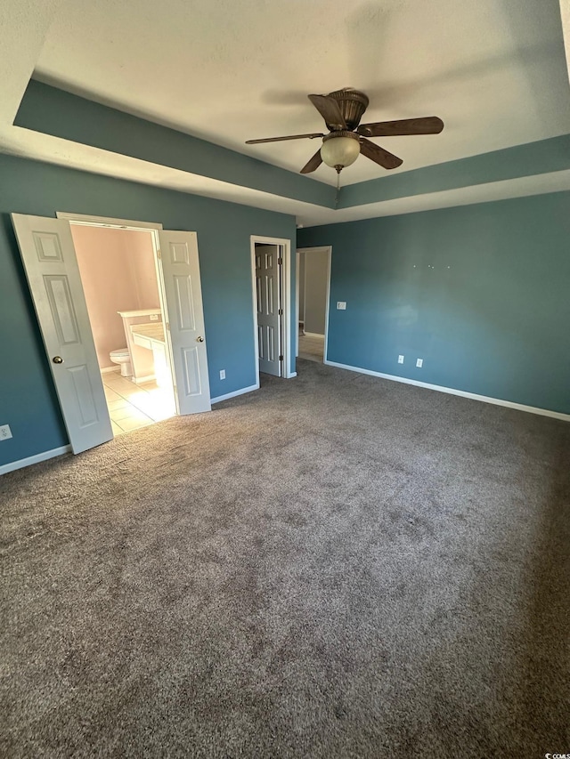 unfurnished bedroom with ceiling fan, a tray ceiling, connected bathroom, and carpet floors