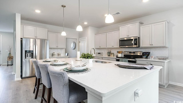 kitchen with stainless steel appliances, sink, a kitchen island with sink, and white cabinets