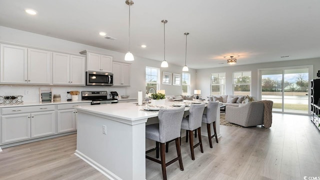 kitchen with a kitchen bar, an island with sink, white cabinets, and appliances with stainless steel finishes