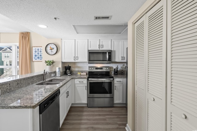 kitchen with appliances with stainless steel finishes, kitchen peninsula, sink, and white cabinets