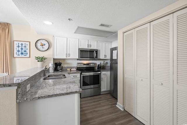 kitchen with sink, light stone counters, appliances with stainless steel finishes, kitchen peninsula, and white cabinets