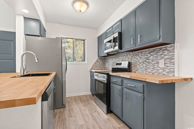 kitchen with light hardwood / wood-style flooring, wooden counters, sink, appliances with stainless steel finishes, and decorative backsplash