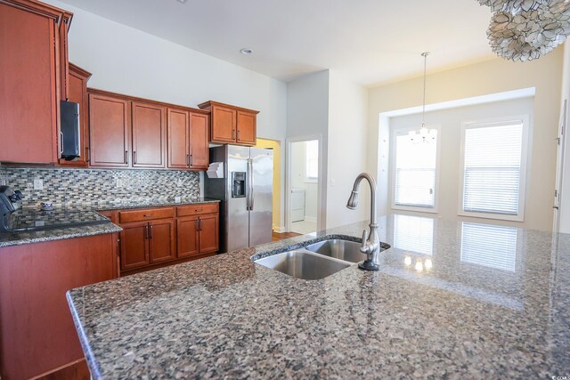 kitchen featuring stainless steel refrigerator with ice dispenser, sink, hanging light fixtures, dark stone countertops, and backsplash