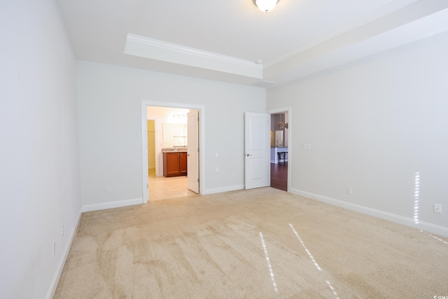 unfurnished bedroom with light colored carpet, ornamental molding, a tray ceiling, and ensuite bath