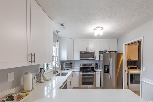 kitchen with appliances with stainless steel finishes, washer / dryer, white cabinetry, and pendant lighting