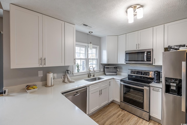 kitchen featuring a textured ceiling, white cabinetry, stainless steel appliances, sink, and hanging light fixtures