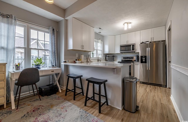 kitchen with kitchen peninsula, appliances with stainless steel finishes, a kitchen breakfast bar, and white cabinetry