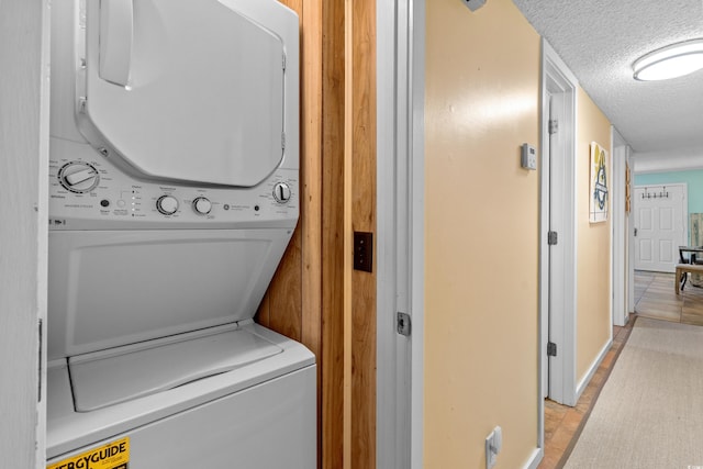 clothes washing area with wooden walls, a textured ceiling, and stacked washer / dryer