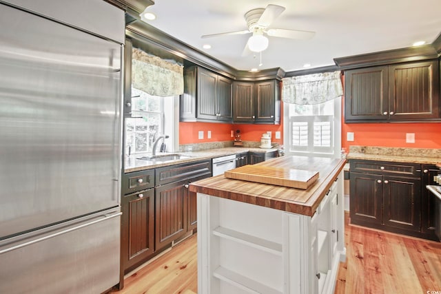 kitchen with built in fridge, a kitchen island, butcher block counters, light hardwood / wood-style floors, and sink