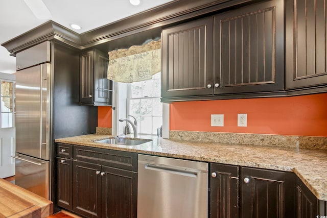 kitchen featuring sink, dark brown cabinetry, light stone counters, and appliances with stainless steel finishes