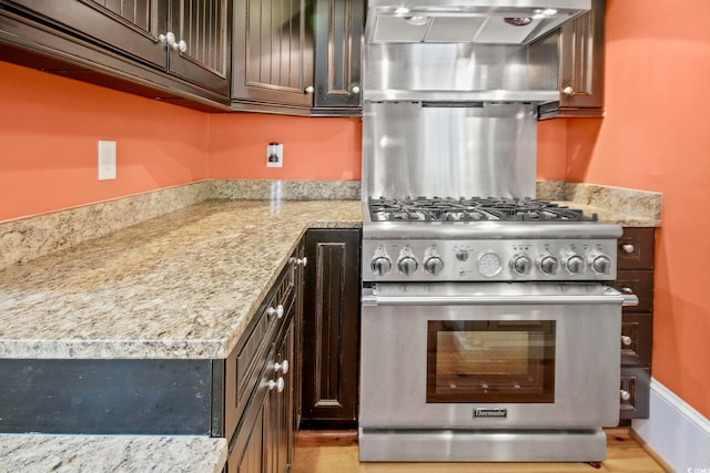 kitchen featuring dark brown cabinets, high end stove, light hardwood / wood-style flooring, and light stone countertops