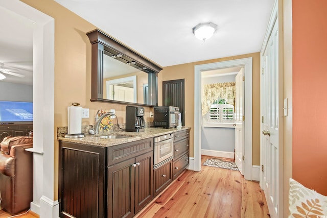 bar with light hardwood / wood-style flooring, ceiling fan, sink, light stone countertops, and dark brown cabinetry