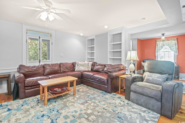 living room featuring hardwood / wood-style flooring, built in shelves, ceiling fan, and a healthy amount of sunlight