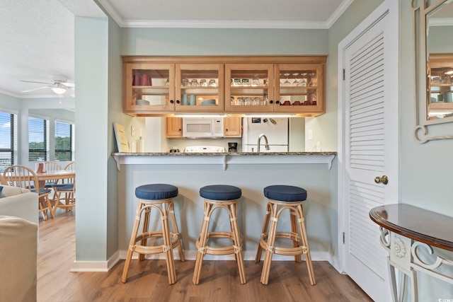 kitchen featuring glass insert cabinets, white appliances, ornamental molding, and wood finished floors