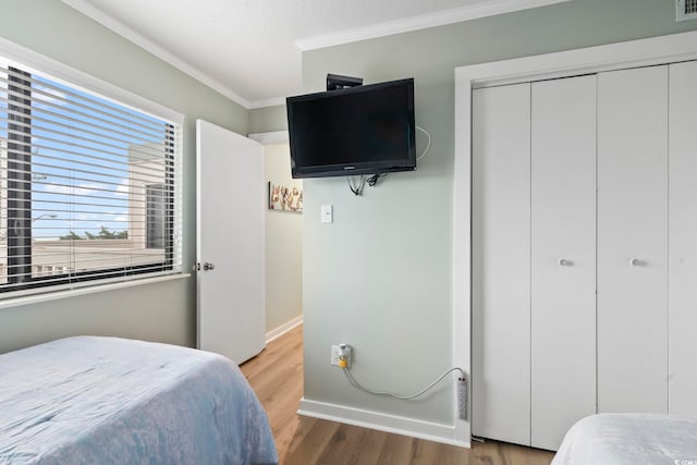 bedroom featuring baseboards, a closet, ornamental molding, and wood finished floors