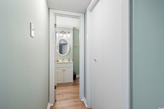 hall featuring light wood finished floors, baseboards, and a sink