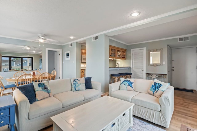 living room featuring light wood-type flooring, visible vents, crown molding, and ceiling fan