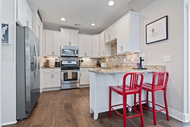 kitchen featuring dark hardwood / wood-style floors, kitchen peninsula, appliances with stainless steel finishes, white cabinets, and light stone counters