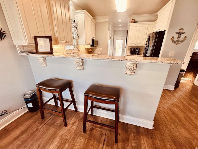 kitchen with white cabinets, black fridge, kitchen peninsula, light stone counters, and a breakfast bar