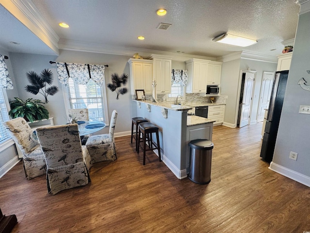 kitchen with decorative backsplash, white cabinets, kitchen peninsula, a breakfast bar area, and stainless steel fridge