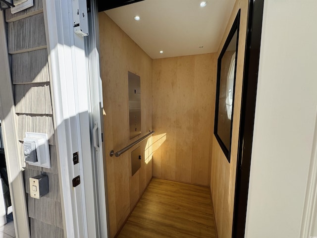 corridor featuring light hardwood / wood-style floors, elevator, and wooden walls