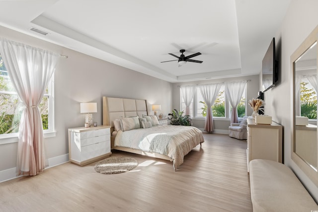 bedroom with ceiling fan, a tray ceiling, and light wood-type flooring