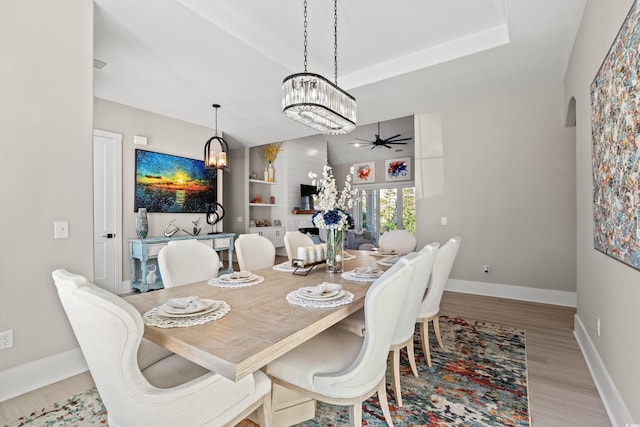 dining area with ceiling fan, a tray ceiling, and light hardwood / wood-style floors