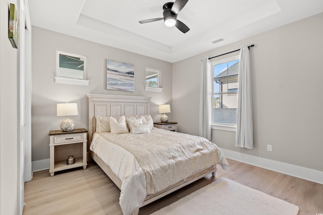 bedroom with a tray ceiling, ceiling fan, and light wood-type flooring