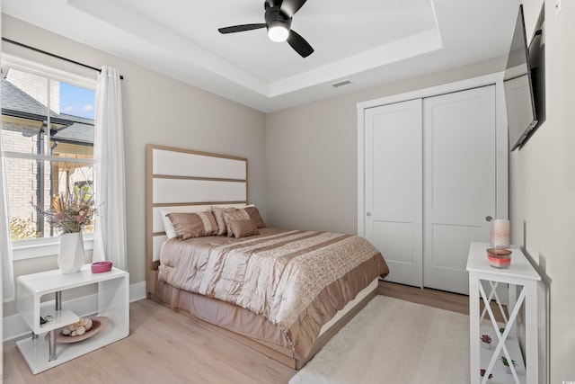 bedroom with a tray ceiling, light hardwood / wood-style flooring, a closet, and ceiling fan