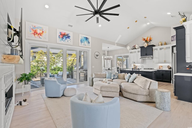 living room with ceiling fan with notable chandelier, high vaulted ceiling, and light hardwood / wood-style flooring